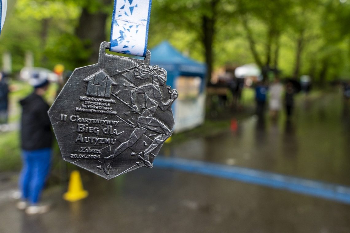 Medal II Charytatywnego Biegu dla Autyzmu z datą 20 kwietnia 2024, w tle mokra od deszczu aleja parku