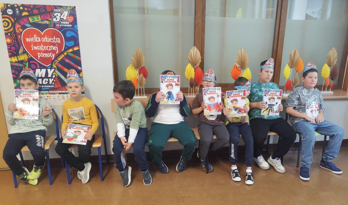 Chłopcy w papierowych koronach „Super Chłopak” siedzą w rzędzie i pokazują certyfikaty