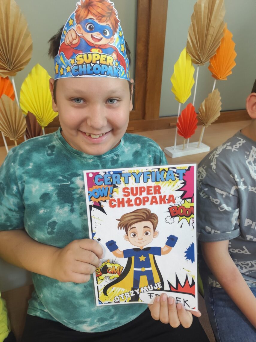 Uśmiechnięty uczeń w koronie „Super Chłopak” trzyma certyfikat Super Chłopaka