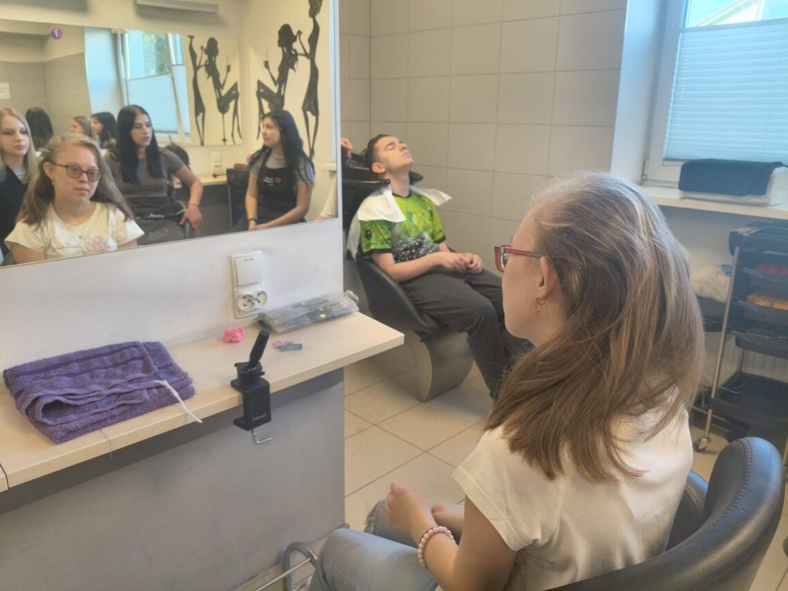 Uczennica w salonie fryzjerskim, w lustrze grupa uczniów